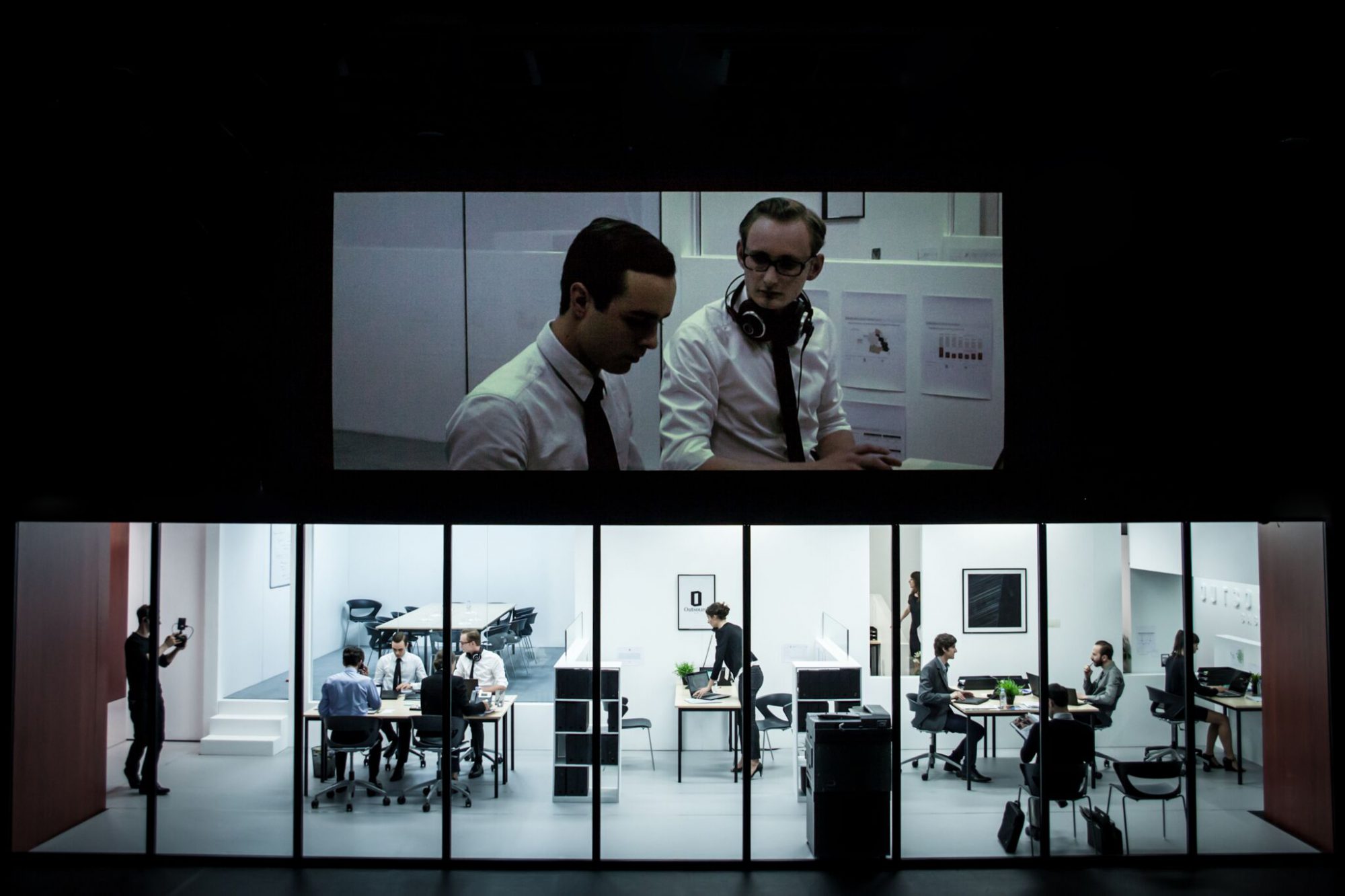 La présence de cameramans sur scène évoque la surveillance et le besoin de justifier en permanence sa place dans le monde du travail actuel.
