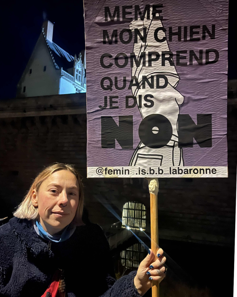 La marche a pris fin au miroir d'eau. Lauriane brandit la pancarte qu'elle a elle-même illustrée, rappelant que le respect du consentement est la clé pour combattre les VSS. 25/11/2025 Photo © Louise Bret