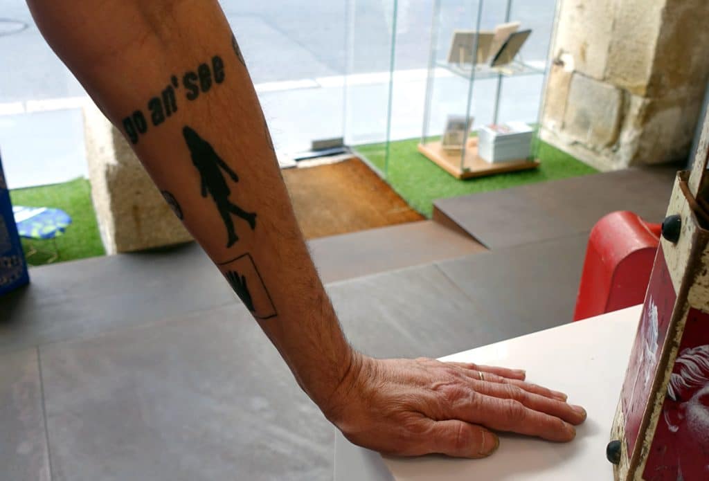 Go an' see, le tatouage sur le bras de Fred Mazère comme une invitation à venir visiter les œuvres de l'expo "So what!"